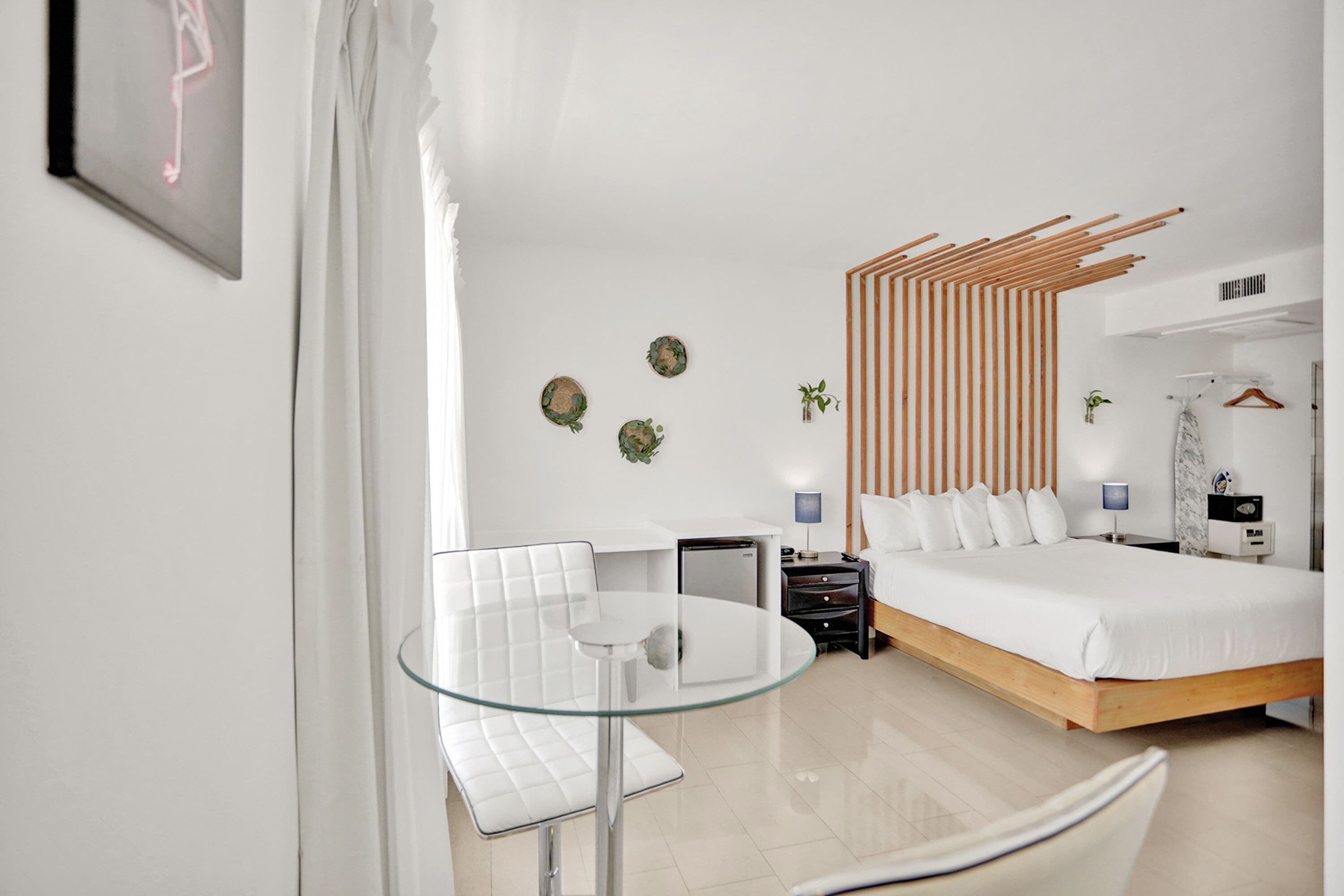A modern hotel room with a bed, bedside tables, a glass table, a chair, and a decorative wooden panel.