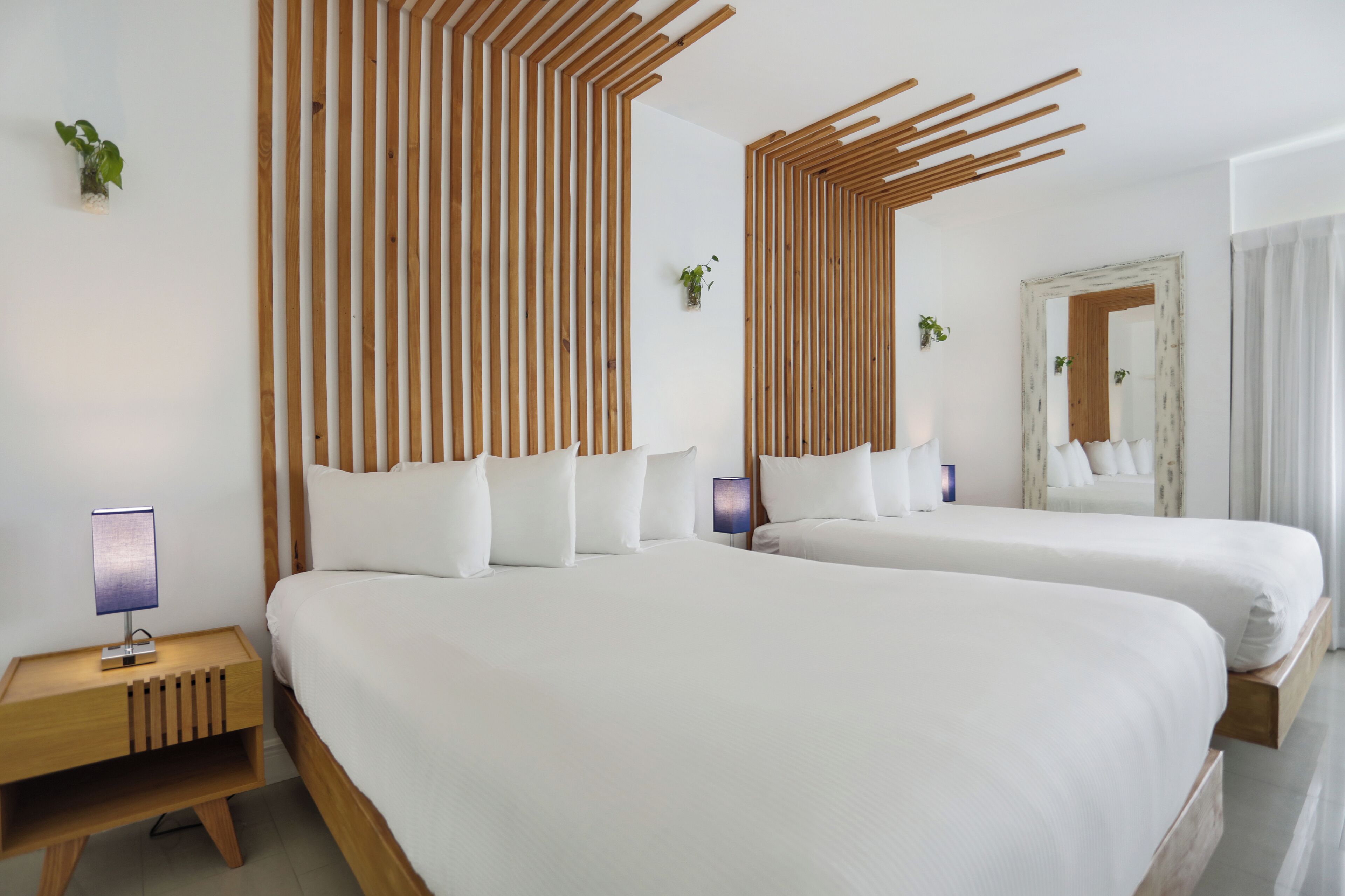 A modern hotel room with two beds, wooden slats on the walls, a nightstand with a lamp, and a mirror with a rustic frame.