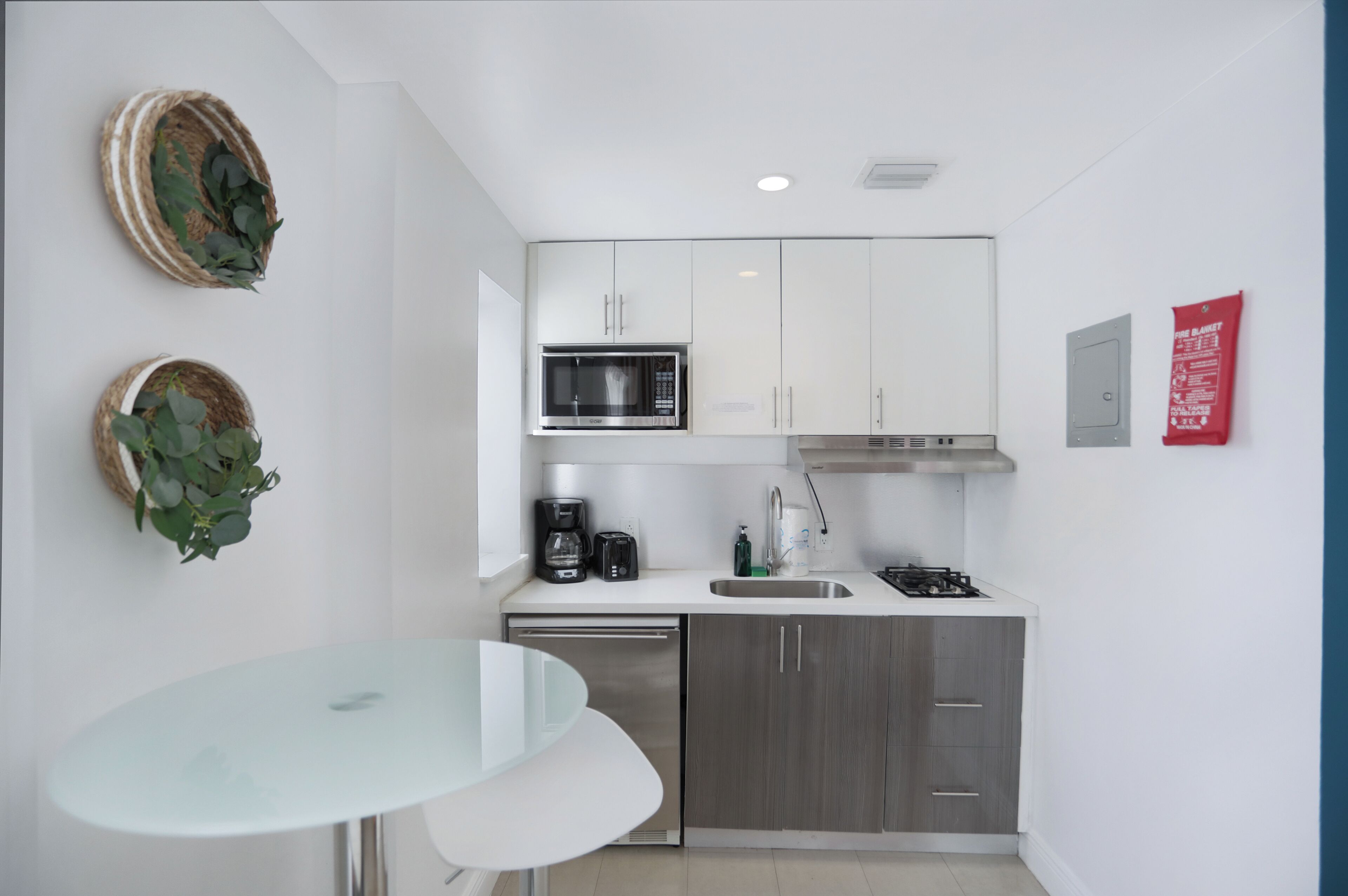 A modern kitchen with white cabinets, a stainless steel microwave, a gas stove, and a dishwasher. There are two wall-mounted baskets with green leaves.