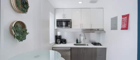 A modern kitchen with white cabinets, a stainless steel microwave, a gas stove, and a dishwasher. There are two wall-mounted baskets with green leaves.
