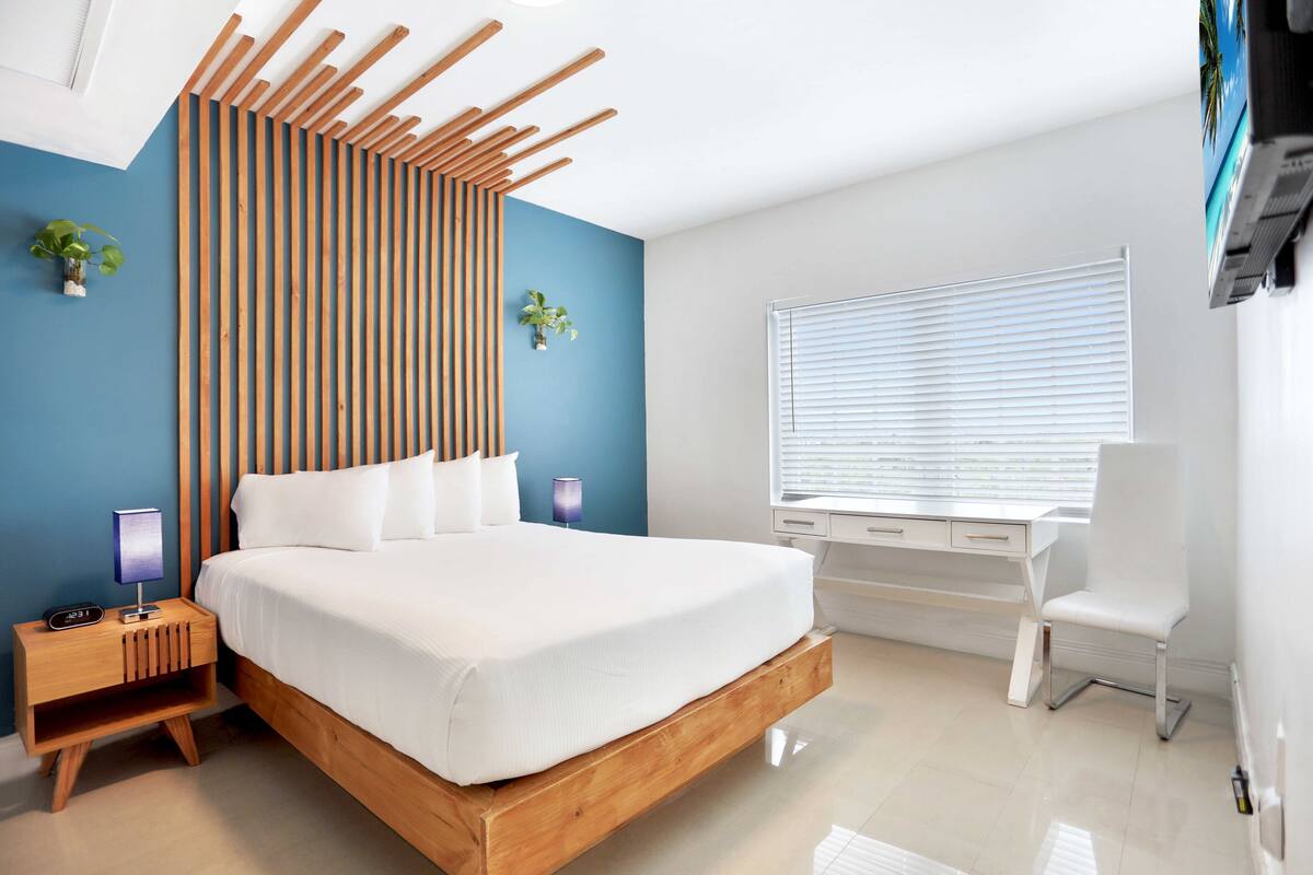 A modern bedroom with a wooden bed frame, a bedside table with a lamp, and a desk with a chair.