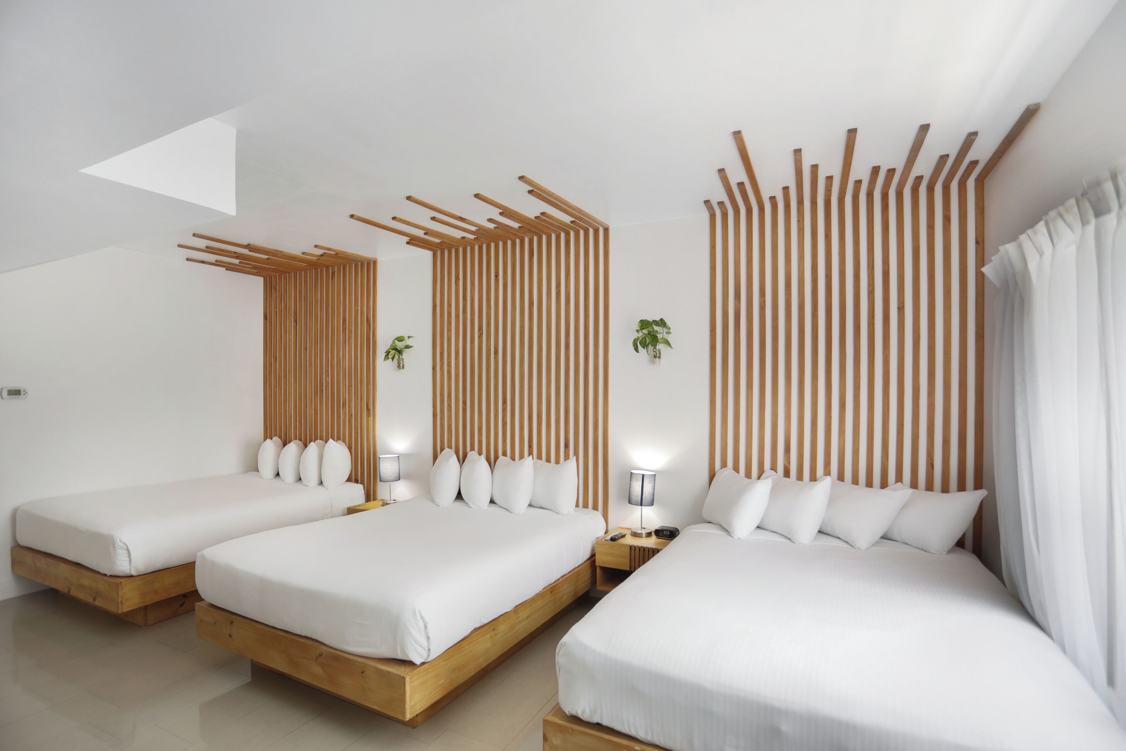 Ein modernes Hotelzimmer mit drei Betten, Holzkopfteilen und einer schrägen Decke.