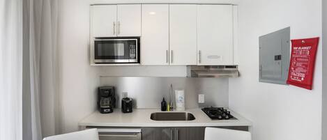 A compact kitchenette with a microwave, coffee maker, sink, and gas stove.