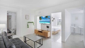 Un salon moderne avec un canapé, une table basse, un téléviseur et un lit dans la pièce adjacente.
