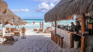 Un bar de playa con sillones de madera y sombrillas de paja, con vista al océano.