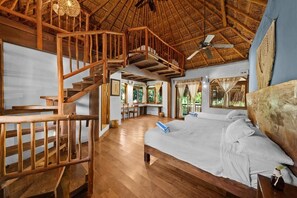 Una habitación amplia con escaleras de madera, una cama grande y un ventilador de techo.