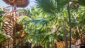 Una escalera de madera conduce a una edificación con techo de paja rodeada de exuberante vegetación tropical.
