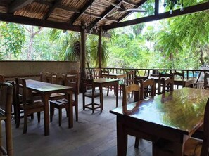 An outdoor dining area with wooden tables and chairs, a thatched roof, and a view of lush greenery. - Playa Canek Hotel Boutique Spa (Mexico)