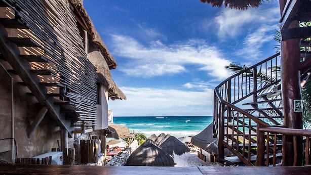 Vista de la playa con una estructura de madera, una escalera que lleva a un balcón y una vista despejada del océano.