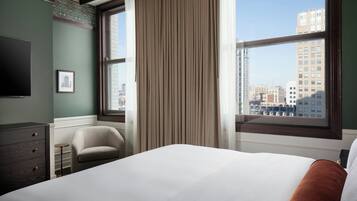 A hotel room with a large bed, a chair, a small table, and a TV on the wall.