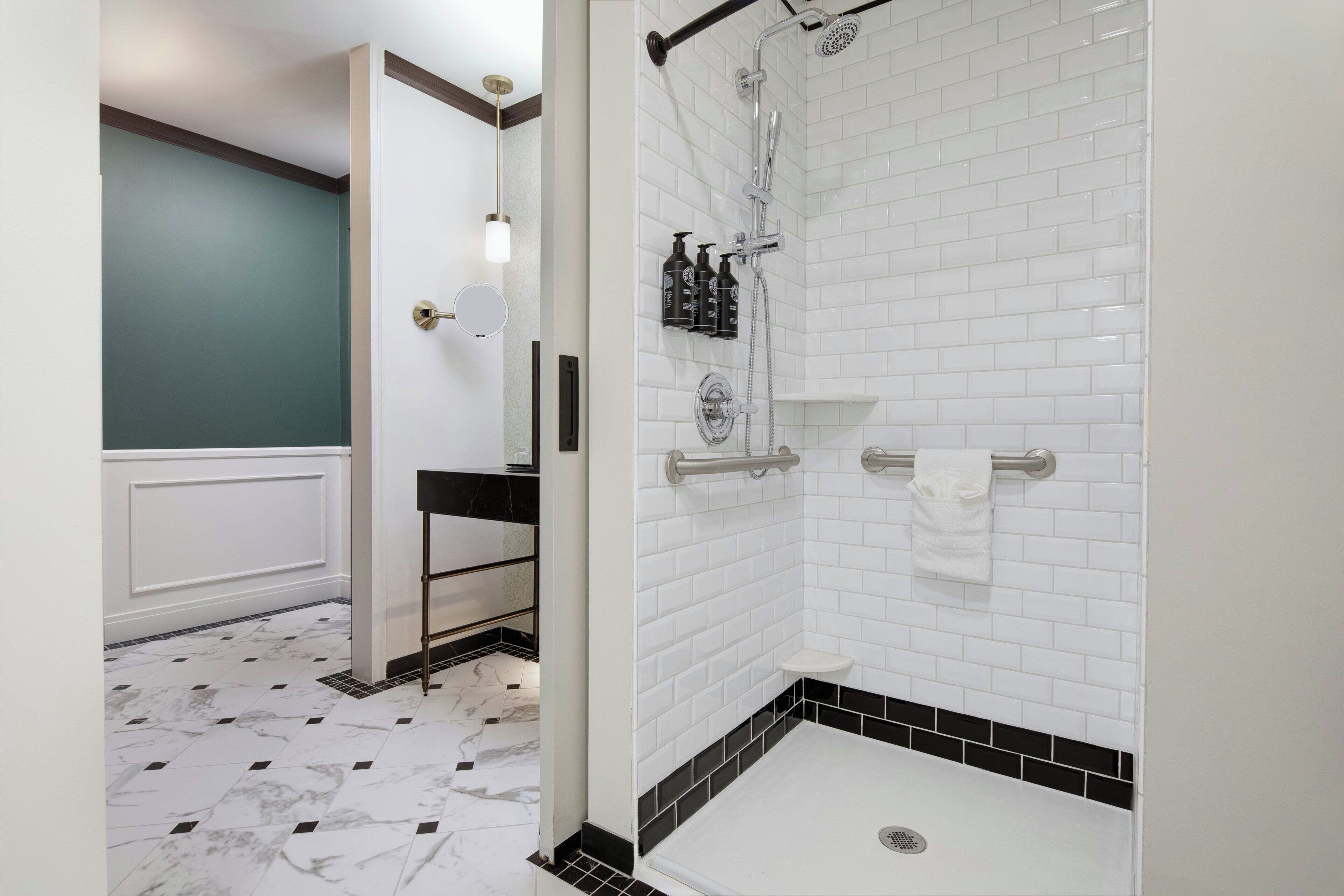 Um banheiro com azulejos brancos tipo metrô, piso quadriculado em preto e branco, chuveiro com chuveiro manual e porta-toalhas.