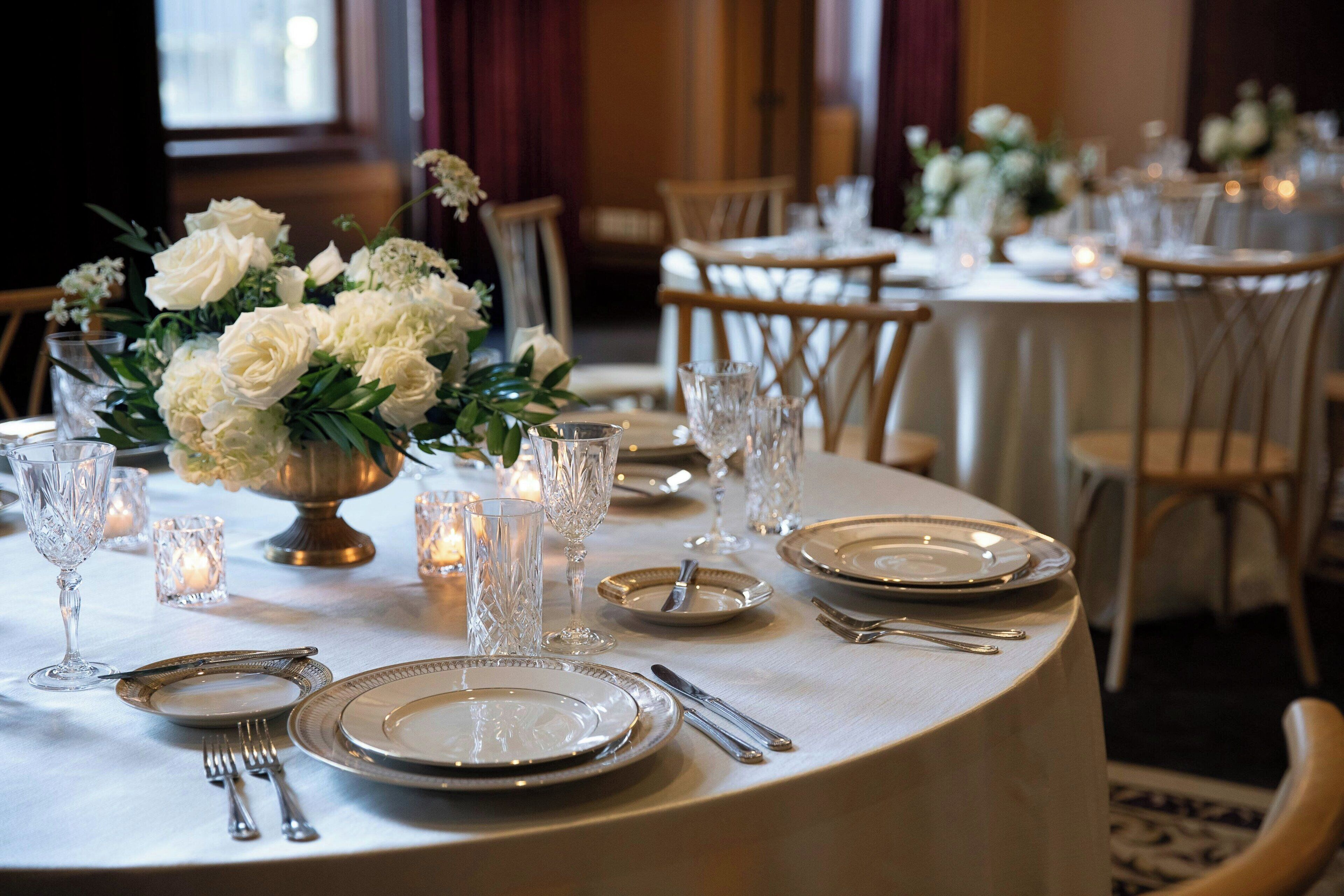Una mesa dispuesta para un evento formal, con manteles blancos, cubertería y cristalería.