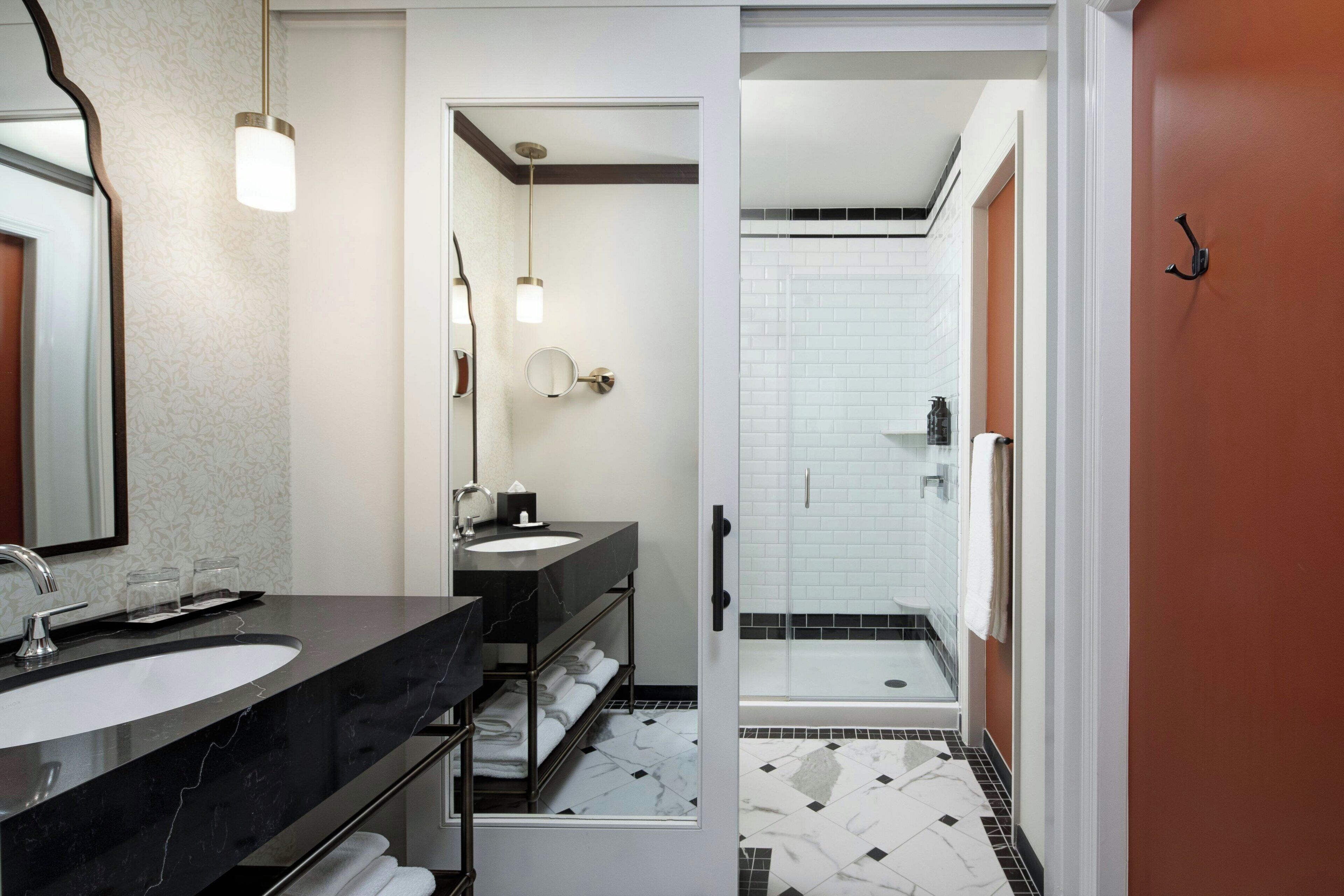 Un baño moderno con lavamanos de mármol negro, cabina de ducha de vidrio y zona de ducha con azulejos blancos.
