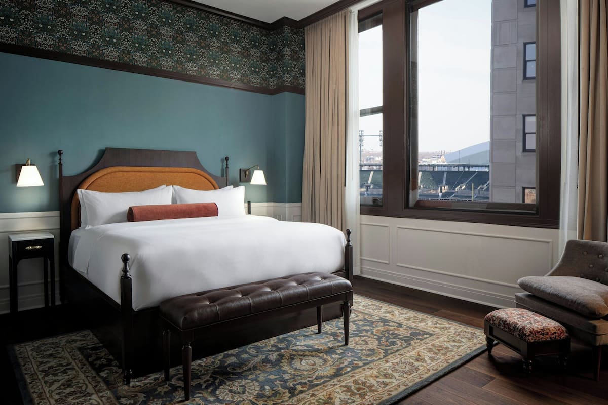 A hotel room with a large bed, a bench, a chair, a nightstand, and a view of a bridge.