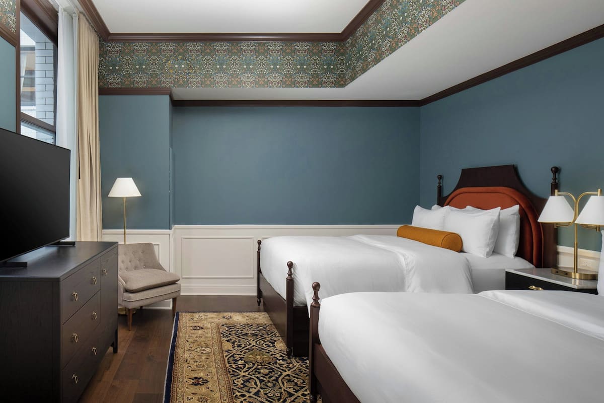 A hotel room with two beds, a dresser, a television, and a lamp.