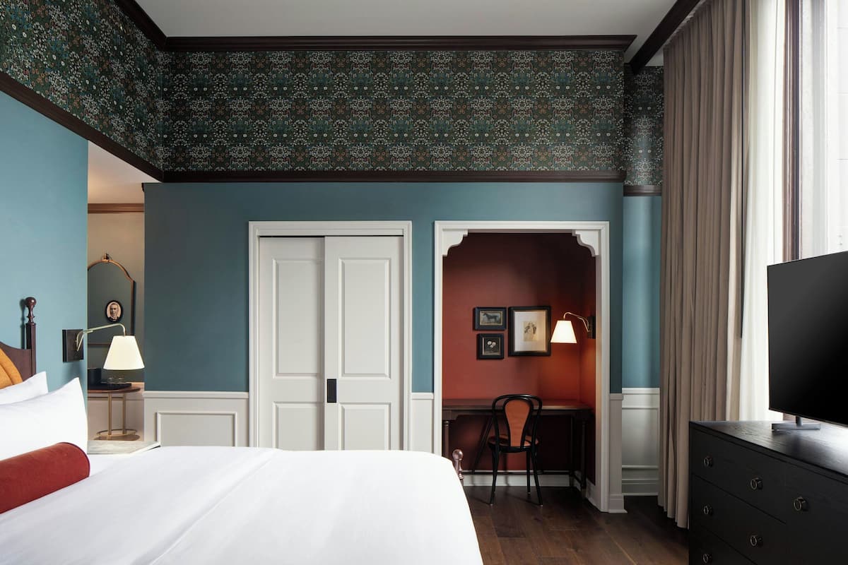 A hotel room with a bed, a desk, a chair, a TV, and a wardrobe.