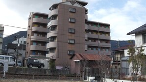 A multi-story residential building with balconies, a visible antenna, and a small fenced area with a ladder. - Sunwell Kotohira (Kotohira)