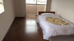 A bedroom with a wooden floor, a bed with a white mattress and a patterned blanket, and a sliding glass door leading to an outdoor area. - Sunwell Kotohira (Kotohira)
