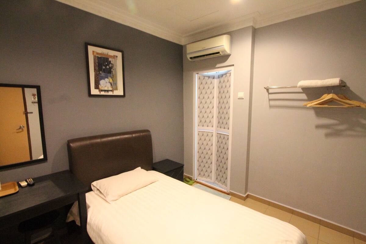 A hotel room with a bed, a desk, a mirror, an air conditioner, a wardrobe, and a towel rack.