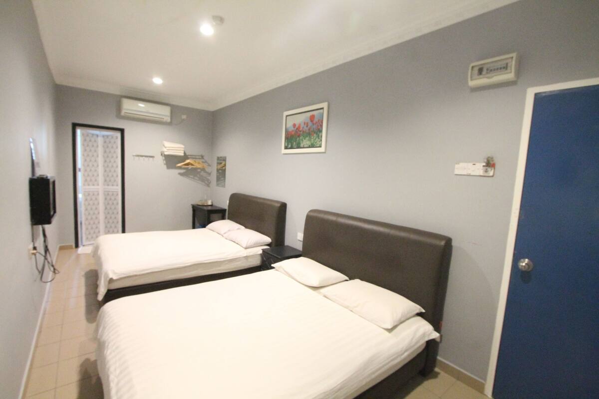 A hotel room with two beds, a wardrobe, a small table, and a wall-mounted air conditioner.