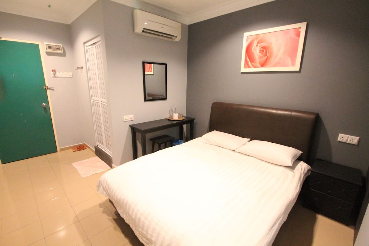 A bedroom with a bed, a desk, a chair, a dresser, and a wall-mounted air conditioner.