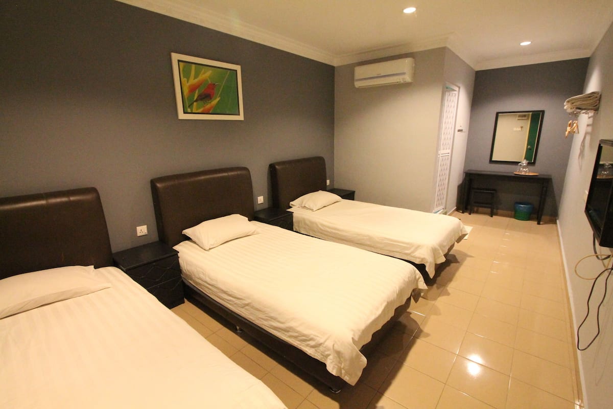 A hotel room with three beds, a small desk, a mirror, and an air conditioning unit.