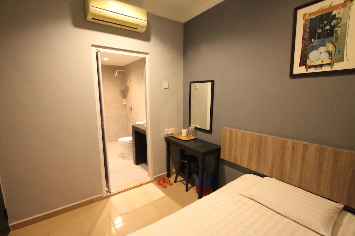 A bedroom with a bed, a desk with a chair, a mirror, and a door leading to a bathroom.