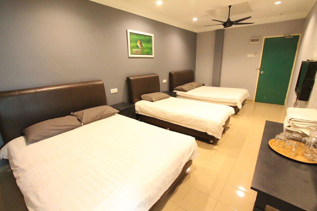 A hotel room with three beds, a ceiling fan, a green door, and a small table with glasses.