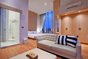 Una habitación de hotel moderna con una cama, un sofá, cabina de ducha de vidrio y un ventanal con vista a la ciudad.