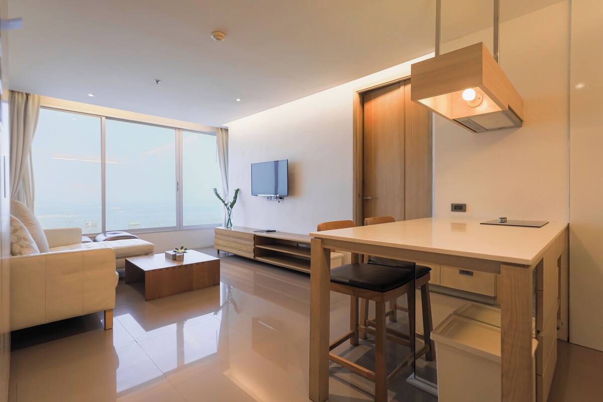 Una habitación de hotel moderna con un ventanal grande, un televisor de pantalla plana, una mesa de comedor de madera y un diseño minimalista.