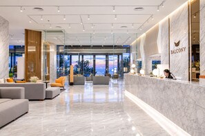 Una moderna hall d'hotel con reception, area salotto e ampie finestre con vista sul tramonto.