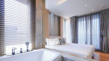 A modern hotel room with a large bathtub, a bed with white bedding, and a large window with blinds.