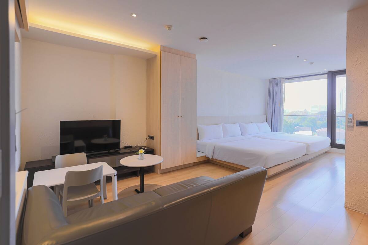 Un hotel moderno con cama, televisor, sofá, una mesita y vistas a la ciudad.