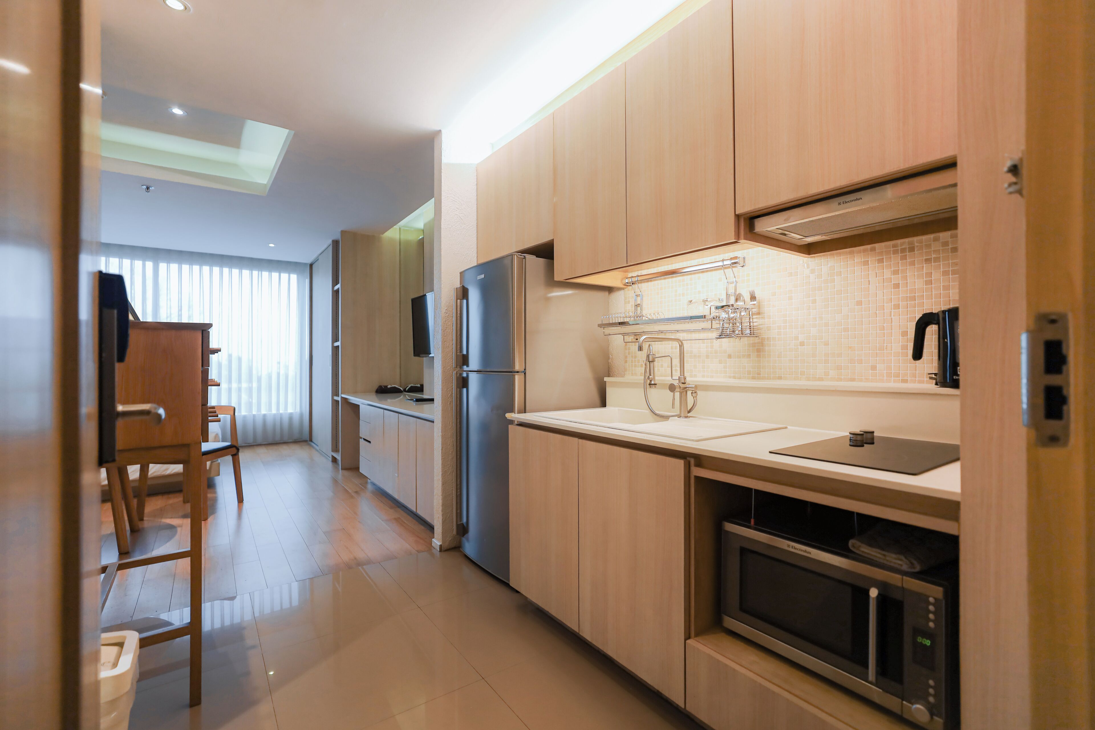 A modern kitchen with wooden cabinets, a stainless steel refrigerator, a microwave, and a sink.