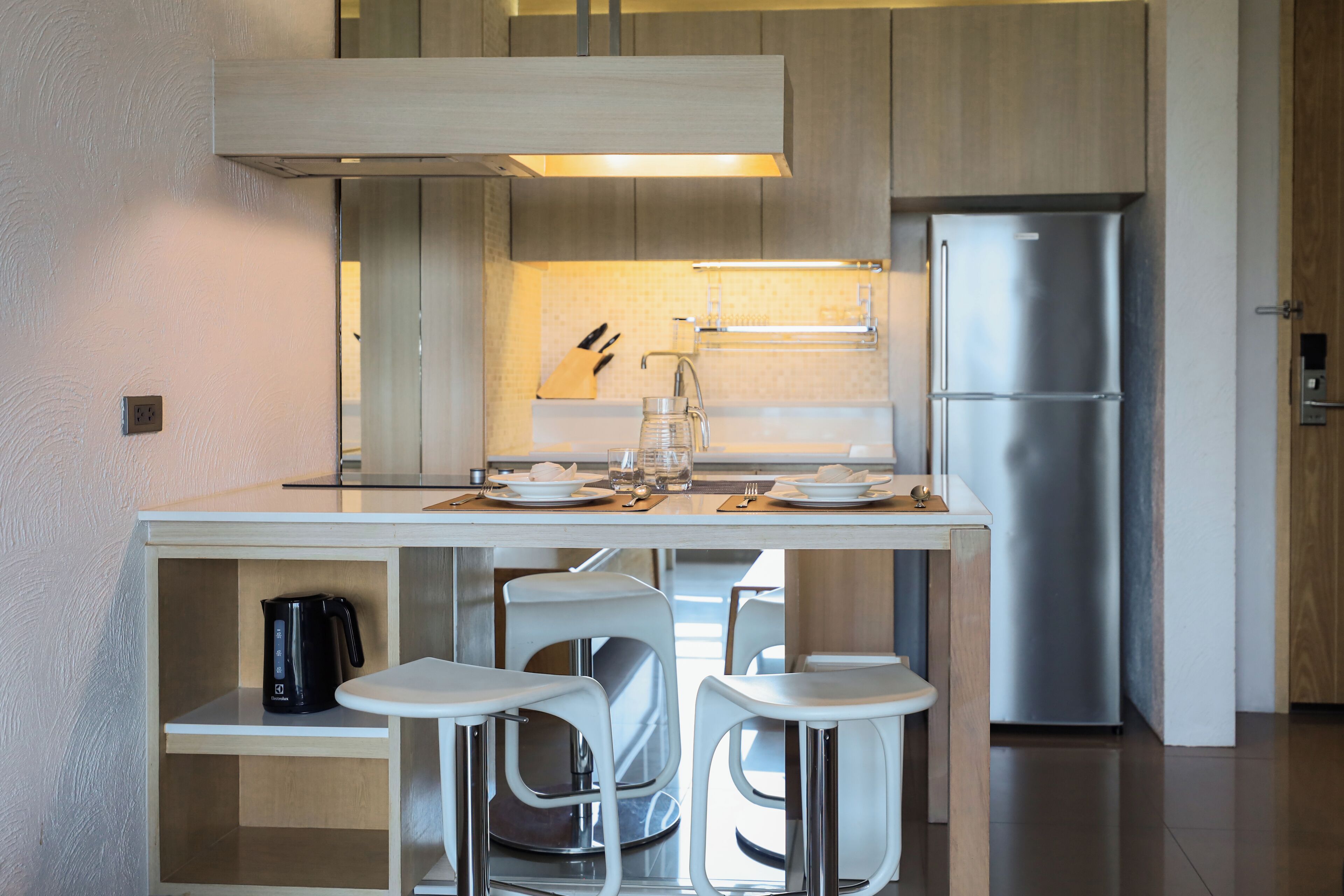 A modern kitchen with a stainless steel refrigerator, white bar stools, and a coffee maker on the counter.