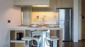 A modern kitchen with a stainless steel refrigerator, white bar stools, and a coffee maker on the counter.