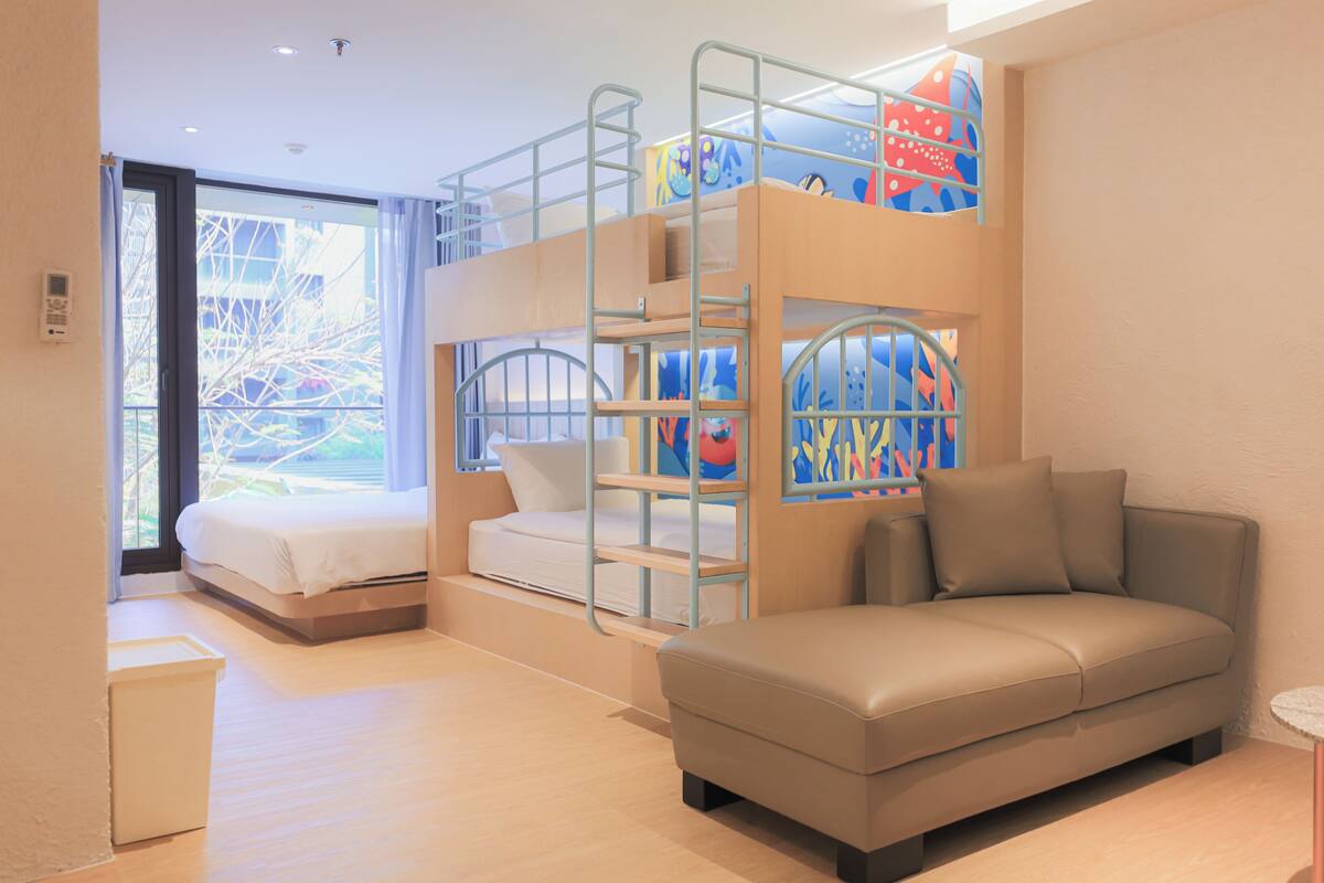 Una habitación con una cama individual superpuesta, un sofá y un ventanal con cortinas.
