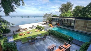 A modern outdoor pool area with a view of the sea, lounge chairs, and a glass-enclosed structure.