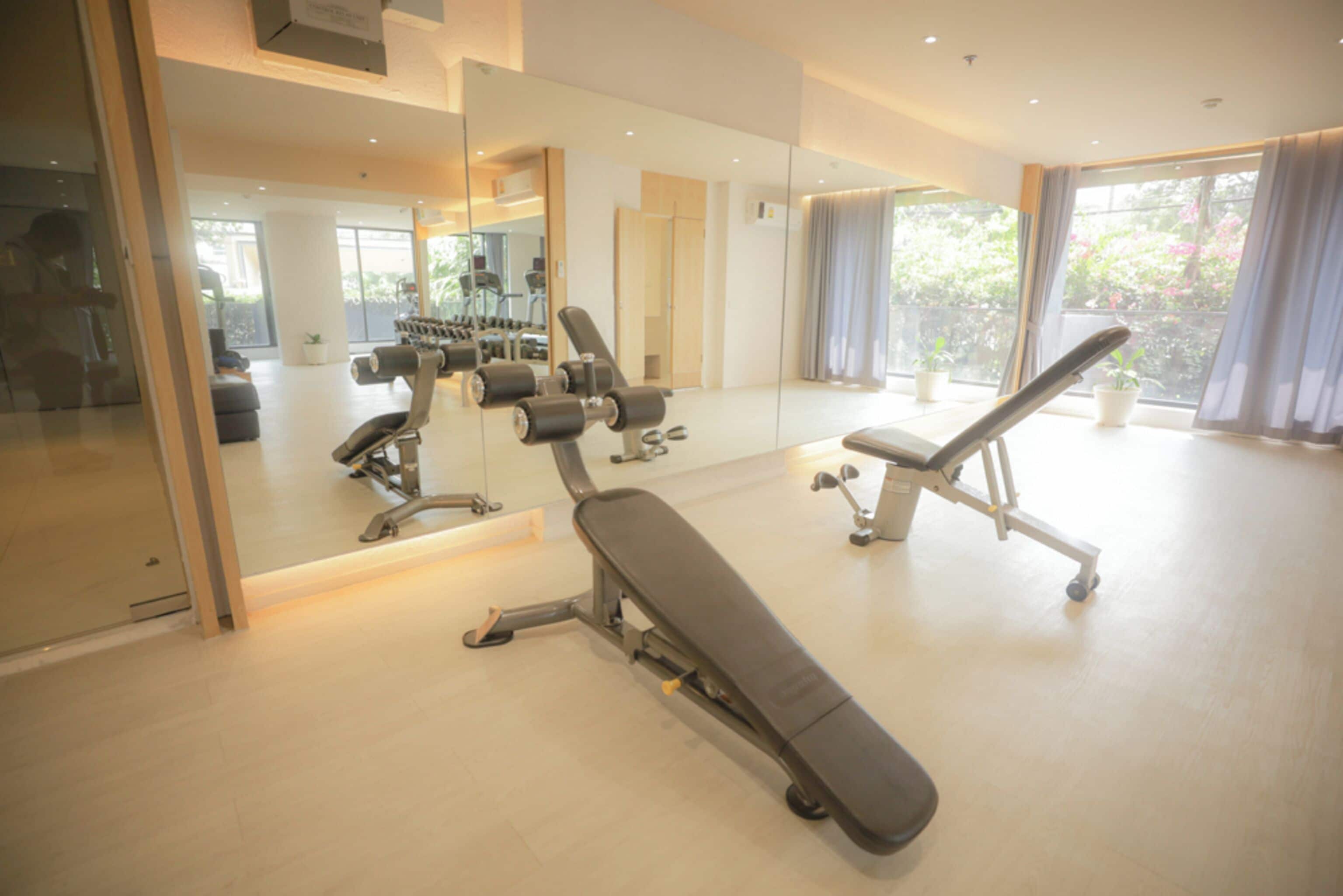 Ein modernes Fitnessstudio mit Trainingsgeräten, großen Spiegeln und Blick auf Grünflächen.