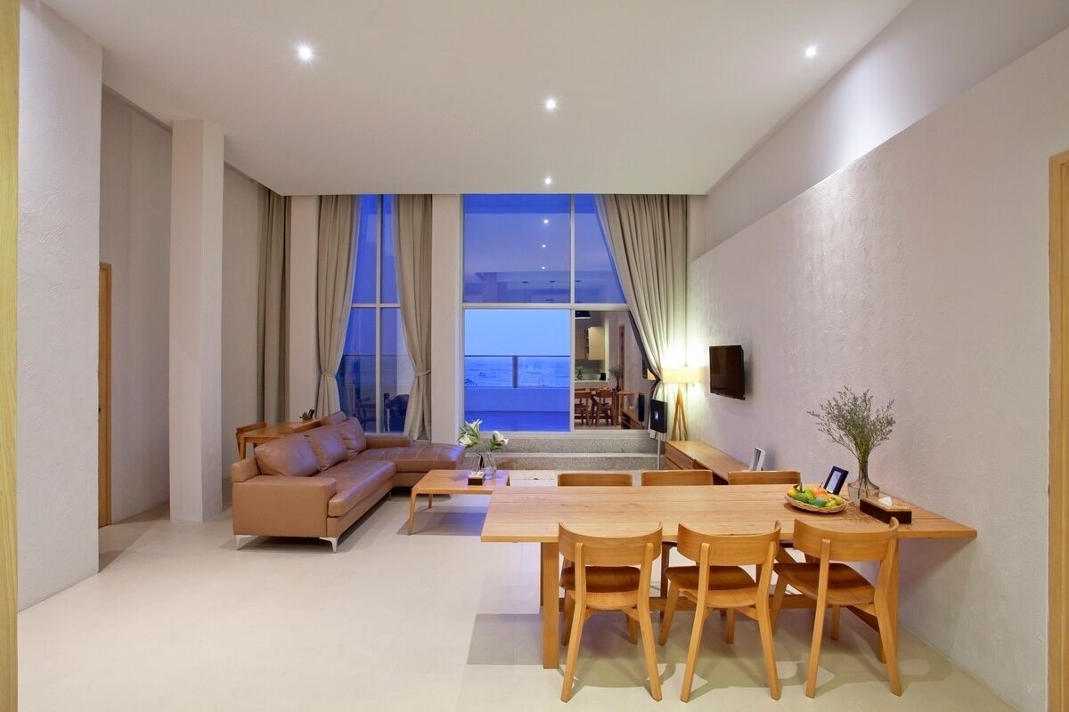 A modern living room with a sofa, dining table, and chairs, large windows with curtains, and a view of the outside.