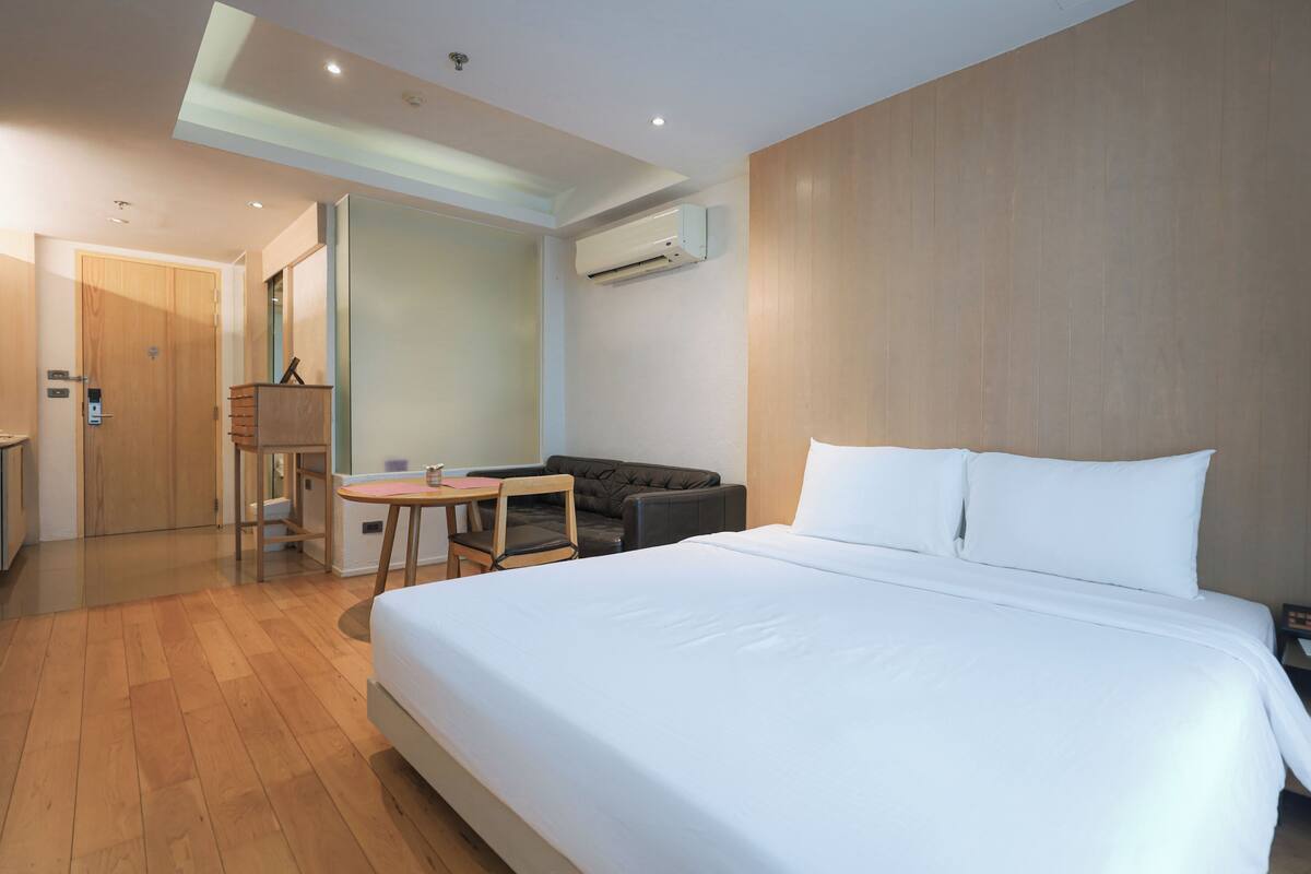 Habitación de hotel con una cama grande, un escritorio, una silla, una mesita, un sofá y un equipo de aire acondicionado.