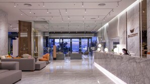 A modern hotel lobby with a marble reception desk, comfortable seating areas, and large windows offering a view of the cityscape.
