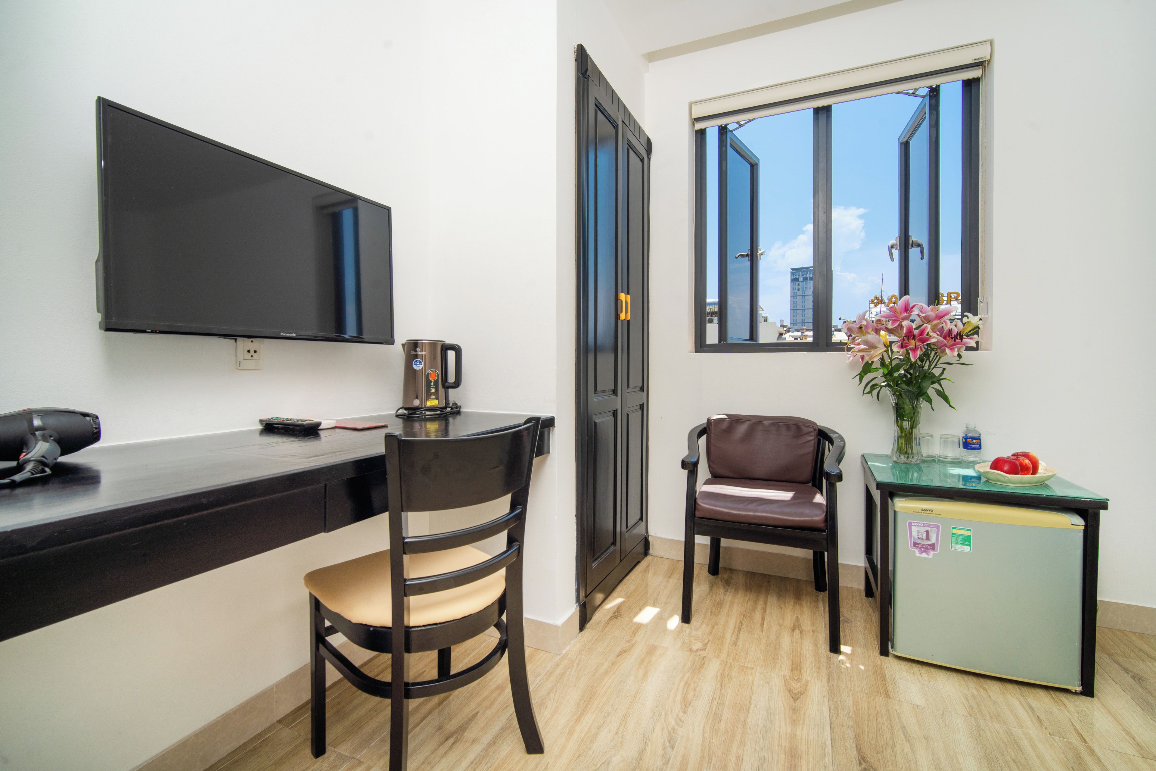 A compact living space with a kitchenette, a dining area with two chairs, a small refrigerator, and a television on the wall.