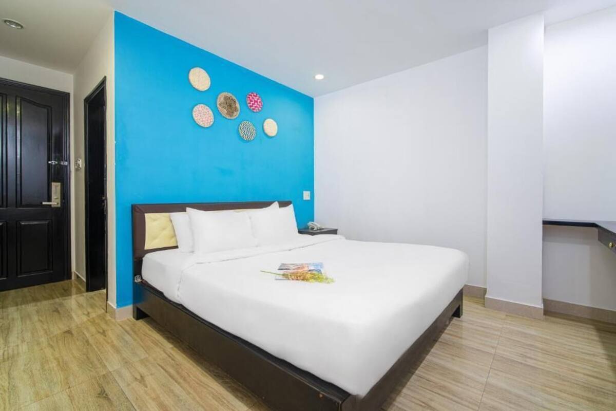 A hotel room with a large bed, a blue accent wall, and a wooden floor.