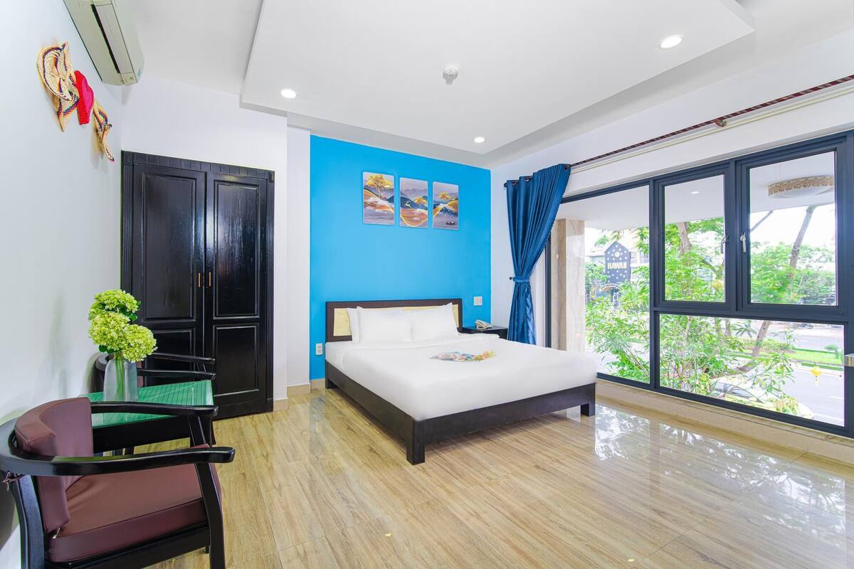 A modern hotel room with a large bed, a desk, and a view of the outdoors.