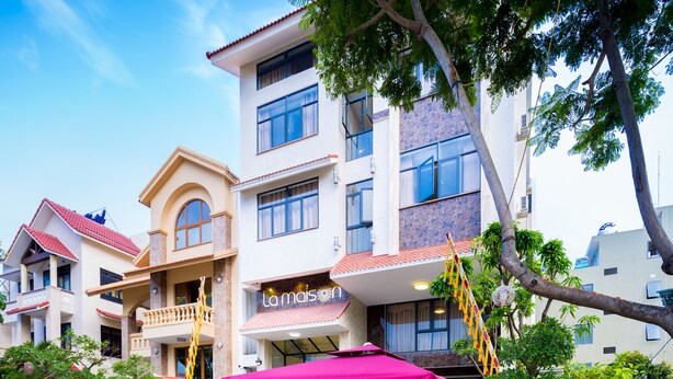 A courtyard with outdoor seating, a building with a sign reading "La Maison," and a tree in the foreground. - La Maison Da Nang Beach (Da Nang)