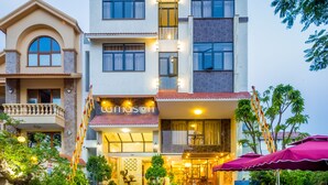 A multi-story hotel with a central entrance, outdoor seating area, and surrounding greenery. - La Maison Da Nang Beach (Da Nang)