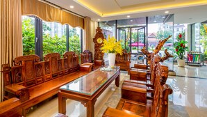 A spacious lobby with a long wooden reception desk, comfortable seating, and large windows offering a view of greenery and buildings outside. - La Maison Da Nang Beach (Da Nang)