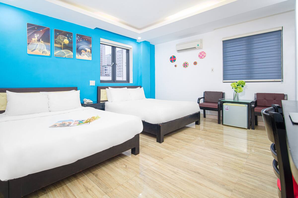 A hotel room with two beds, a desk, a chair, and a small fridge.