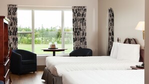 A hotel room with two beds, a small table, a chair, and a view of the outdoors. - Brackley Beach Northwinds Inn and Suites (Brackley Beach)